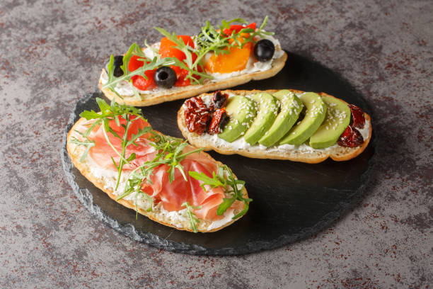 istock Delicious bruschetta with arugula, ham, vegetables, cream cheese close-up on a slate board on the table. Horizontal 1949680248