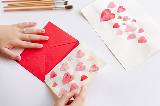 A closeup of a person crafting paper hearts with pencils on an envelope for Valentine's day