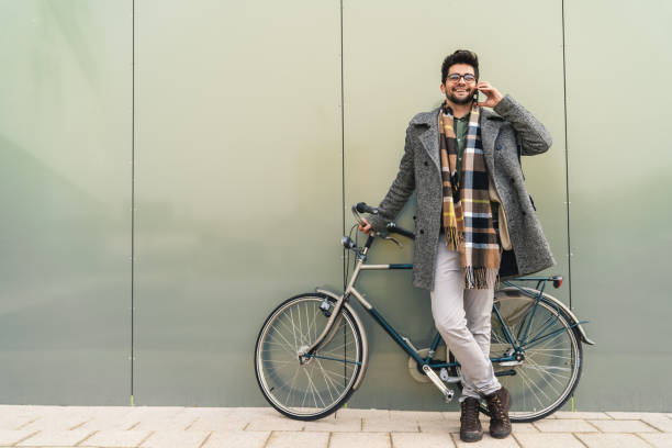 istock Cheerful man with glasses having a phone call conversation while standing next to his bike 1949787524
