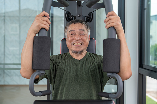 Elderly, Retired or Senior Asian man using pull-down machines to build muscle in a gym or fitness center for good health.