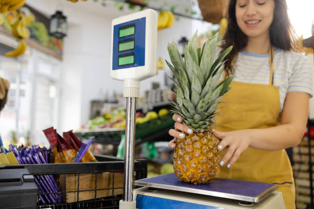 Young saleswoman in the grocery store weighing pineapple.