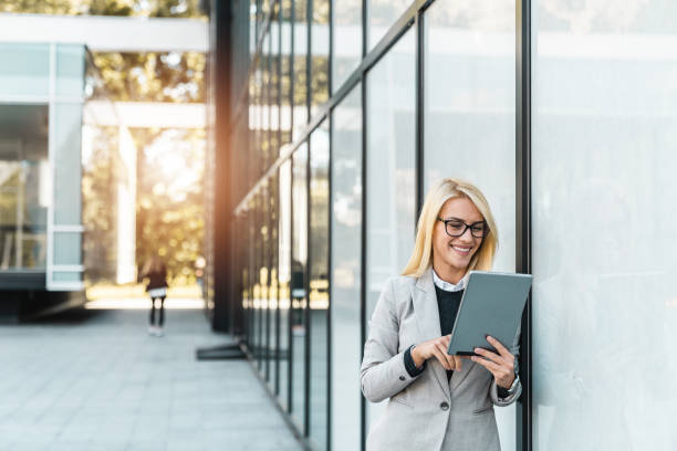 istock Happy smiling businesswoman using digital tablet while standing outside the office building 1949823937