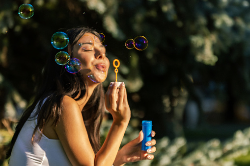 Beautiful young lady is playing with bubbles at sunset.