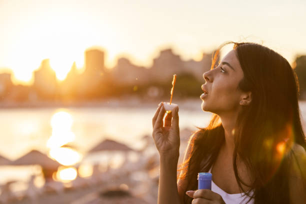 Beautiful young lady is playing with bubbles at sunset.