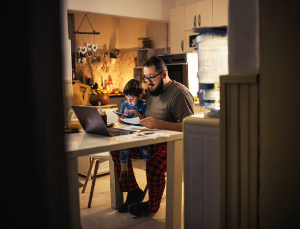 young dad uses laptop and pays bills while son tries to distract him