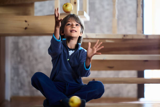Little white boy juggles apples at home.
