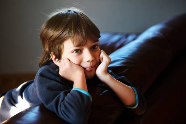 istock Young boy with his hands propping up his head, sitting  on couch. 1949882424