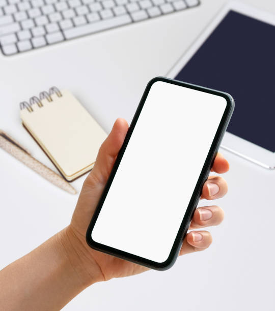 istock Mockup mobile app digital organizer. Hand holding phone with blank screen in front of diary, digital tablet and pc on the desk. 1949886777