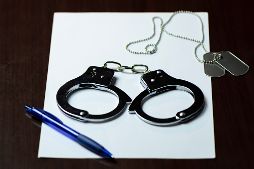 Handcuffs and an army badge on white paper, with a blue pen lying nearby