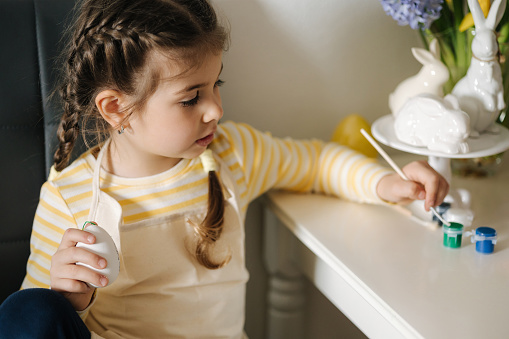 Easter holiday at home, adorable little girl painting eggs in kitchen. High quality photo