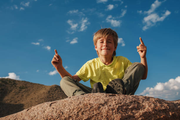 Boy sitting in meditation pose on rock in the mountains