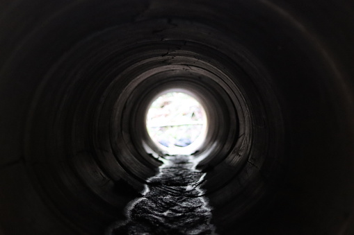 View through a round concrete tunnel carrying a stream beneath a road