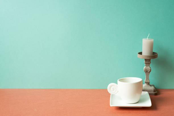 White coffee cup with candle on red table. mint green wall background