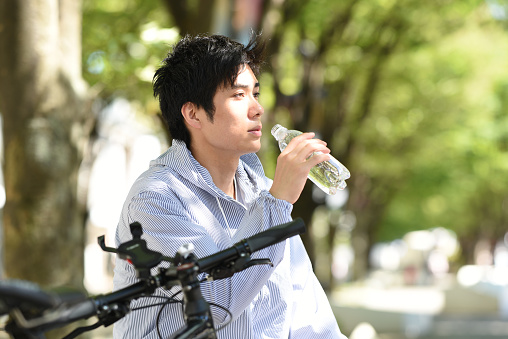 A young Asian man gets off his bike and takes a break while rehydrating.