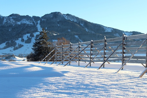 Wintery, snow-covered landscape near Nesselwang (Ostallgäu, Bavaria). In the foreground a wooden snow fence, in the background the mountains (Alpspitze). Winter sports region.