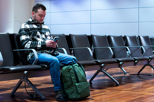 Man with smart phone and luggage waiting in airport departure area. Travel concept.