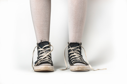 Old blue sneakers hipster style on girl legs in over the knee socks, on a white background