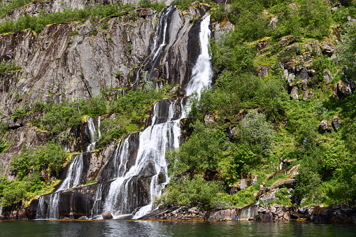 A close-up view of a waterfall in Trollfjorden, Lofoten, Norway, where water streams over moss-covered rocks into the fjord