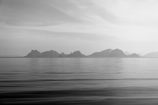 A grayscale scene where the gentle light bathes the silent fjords and mountain outlines of Lofoten, Norway, in a tranquil display