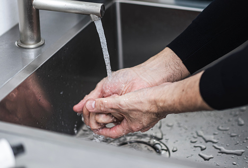 A middle-aged man washes his hands with tap water in the bathroom.