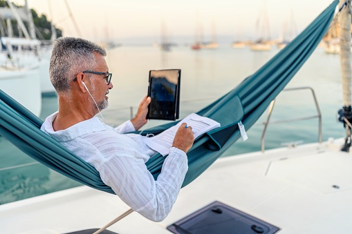 Businessman working while lying down on a hammock on a sailboat