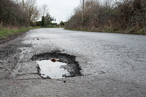 Deep road pothole filled with rainwater. Already filled once, the pot hole is a hazard to cars and other vehicles on this British rural road.