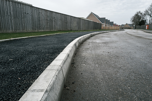 Newly laid asphalt on a pedestrian walk way leading to a new bungalow housing development in the UK. The new road is seen dirty and slippery due to construction vehicles.