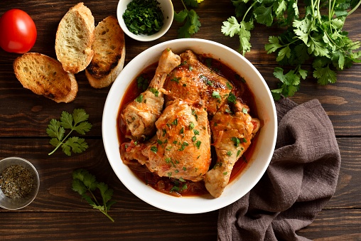Georgian chicken stew with tomatoes and herbs (chakhokhbili) in bowl over wooden background. Baked chicken meat with tomato vegetable gravy. Healthy eating. Top view, flat lay
