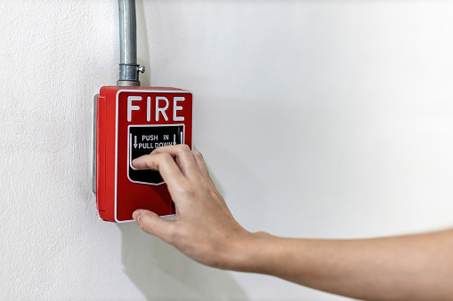 Woamn or worker pushing fire alarm on the wall. A fire! or Emergency case at the factory building. Emergency of Fire alarm or alert or bell warning equipment