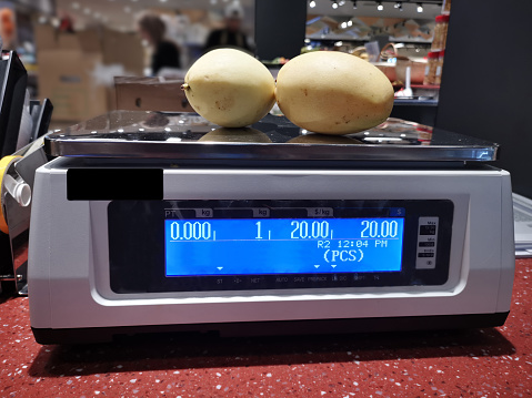 Weighing scale at workplace - weighing fresh mango in supermarket fruit section
