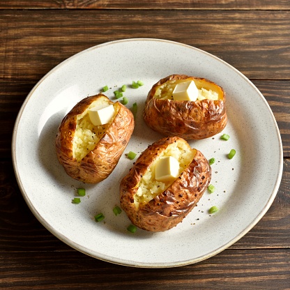 Oven baked potato with butter on white plate on wooden table. Close up view