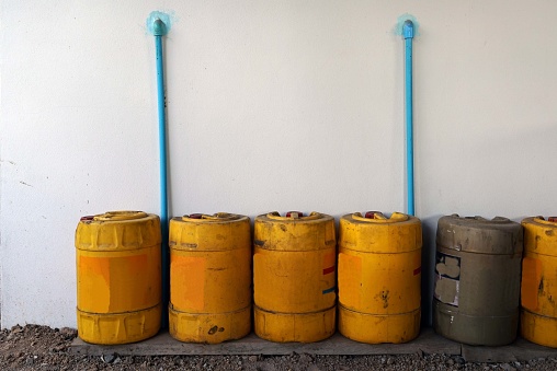 A yellow plastic fuel gallon in a row on ground beside the wall of a building.