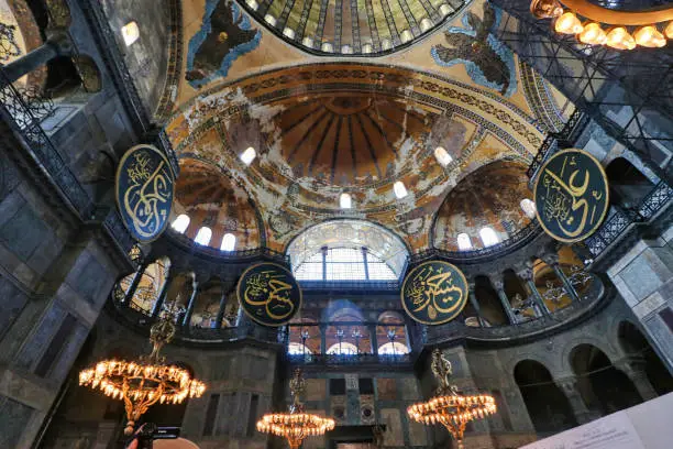 Grand Chandeliers with depictions of angels on the vaulted dome and arches inside the Hagia Sophia - landmark byzantine church built by Justinian in 537 AD in Istanbul, Turkey