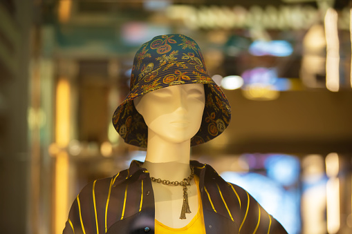 A female mannequin in a Panama hat behind the glass of a store window.