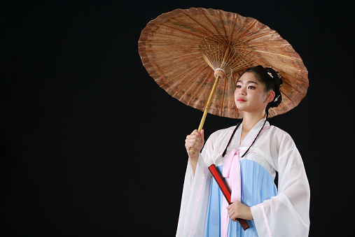 Asian woman wear a traditional dress costume holding red fan and umbrella on hand to celebrate on Chinese festival.
