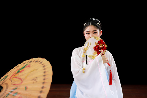Asian woman wearing traditional Chinese dress and holding a hand fan with a black background. Happy Spring Festival, Chinese New Year concept