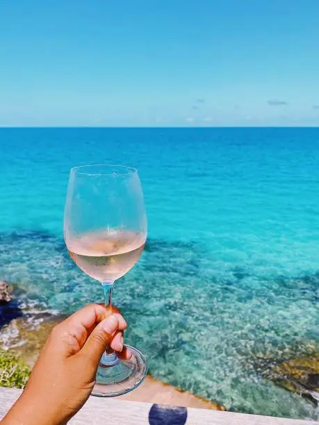 One person holding a glass of wine on a table overlooking the ocean