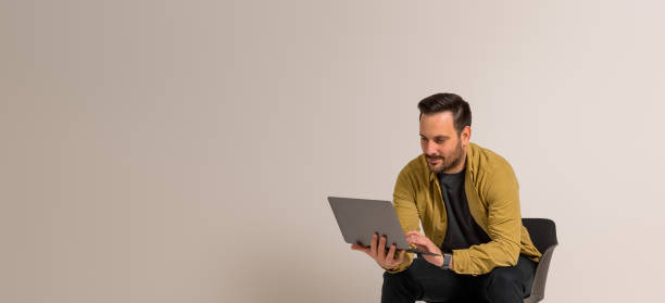 istock Confident young businessman working over laptop while sitting on chair against white background 1950189569