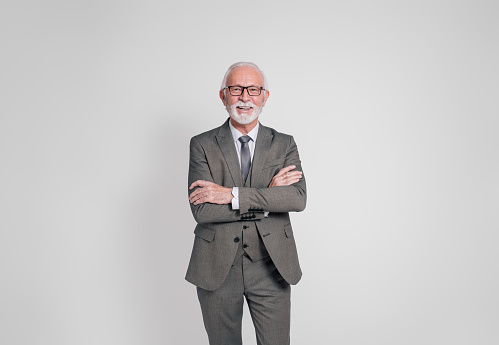 Portrait of smiling confident elderly businessman with arms crossed standing on white background