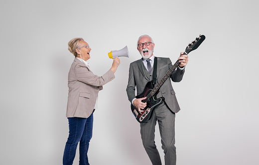 Senior businesswoman singing through megaphone and businessman playing guitar on white background