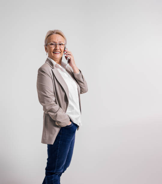 istock Elderly female professional talking over mobile phone and smiling at camera over white background 1950201679