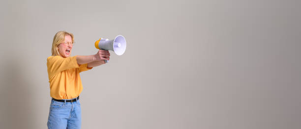 furious female activist with eyes closed shouting over megaphone against isolated white background - boegbeeld model stockfoto's en -beelden