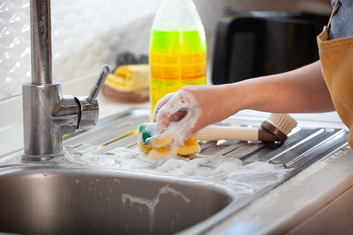 Woman cleaning kitchen cabinets with sponge and spray