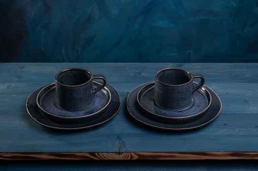 Two empty cups with saucers and plates on wooden blue table. Low Key.