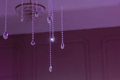 Crystal beads hang from the ceiling, bathed in a soft purple light. The glistening crystals and muted background create a mystical, elegant ambiance.
