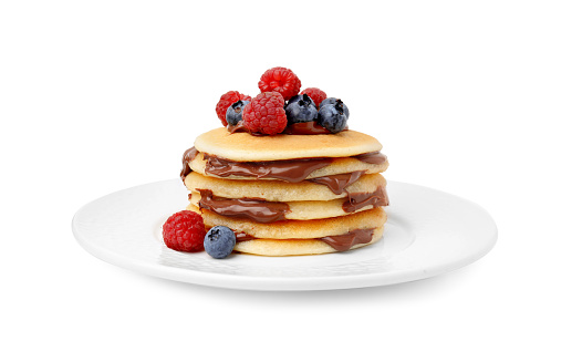 Stack of tasty pancakes with chocolate spread and berries isolated on white