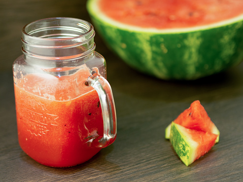 Fresh watermelon smoothie in a glass mug and slices of watermelon on a wooden background