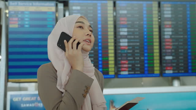 The Muslim woman is checking the flight information on the boarding board displaying departure times at the airport.