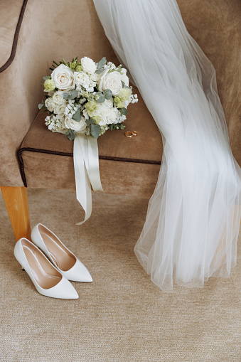 White heels, a lush bouquet, and a bridal veil set a serene, intimate scene for a wedding day. Concept for wedding preparation or bridal boutique.
