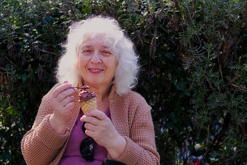 An elderly, curly, gray-haired lady eats ice cream from a waffle cone.